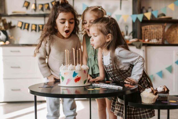Girls blowing candles from birthday cake on table
