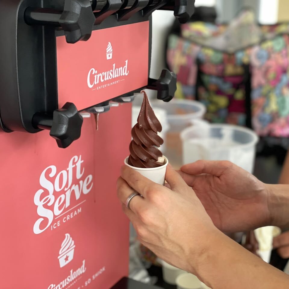 Freshly dispensed chocolate soft serve ice cream in white cup from pink soft serve machine at event